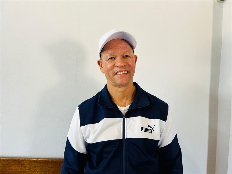 A man wearing a white cap and a Puma jersey stands in front of a plain white background.