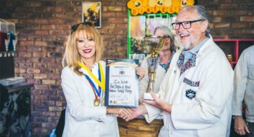 A man and woman wearing white outfits pose with a certificate during an event.