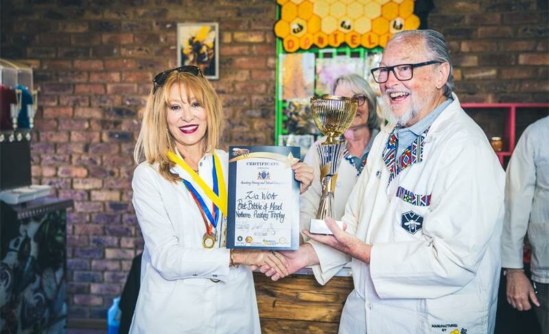 A man and woman wearing white outfits pose with a certificate during an event.
