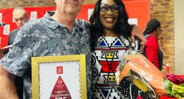 SANBS donor recognised with a framed certificate, pictured with a woman holding flowers at the awards ceremony.