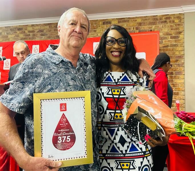 SANBS donor recognised with a framed certificate, pictured with a woman holding flowers at the awards ceremony.