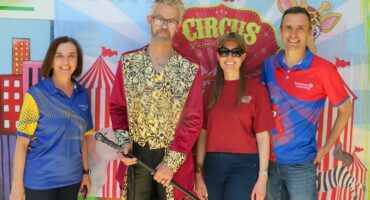 Four people, dressed in formal attire, stand together smiling for a photo in front of a backdrop displaying the word circus at an event