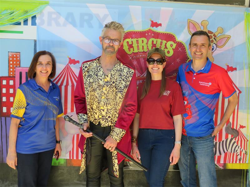 Four people, dressed in formal attire, stand together smiling for a photo in front of a backdrop displaying the word circus at an event