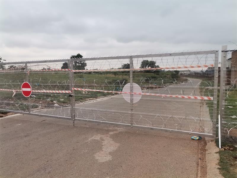 An access control gate installed on a public road, with barbed wire and barrier tape red and white.