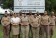 Boksburg Correctional Services officials, dressed in brown correctional uniforms, stand behind the Boksburg Correctional Services signage.