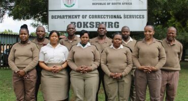 Boksburg Correctional Services officials, dressed in brown correctional uniforms, stand behind the Boksburg Correctional Services signage.