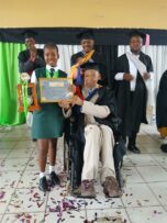 The George Mbilase Primary School top achiever Tshegofatso Fenyane accepting her dux award from a man on a wheelchair, principal Joseph Nhleko, with three men looking on