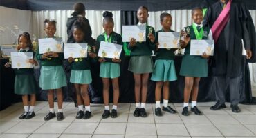 A group of learners in school uniform with a man in academic gown and cap