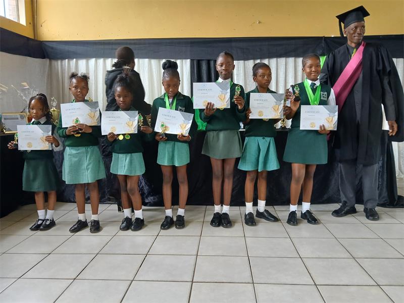 A group of learners in school uniform with a man in academic gown and cap