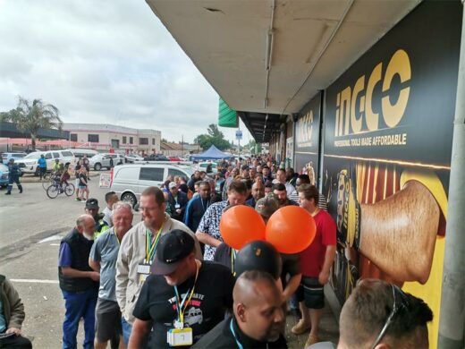 A group of people, mostly white men waiting in line outside a hardware store.