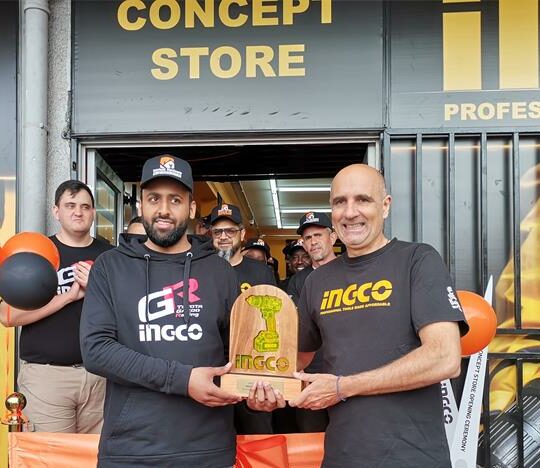 Witfield Hardware owner, Shabbeer Karolia and Ingco power tools South Africa managing director Angelo Angelos standing in front of a newly opened store, with balloons and a few people behind them.