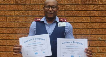 Nurse holding two certificates with brown brick wall background.