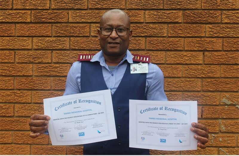 Nurse holding two certificates with brown brick wall background.