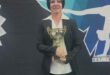 Coach of the year Colleen Jooste posing for a photo with a logo of the club in the background