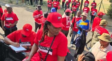 A group of protesters in red union t-shirts marching outside offices.