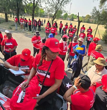 A group of protesters in red union t-shirts marching outside offices.