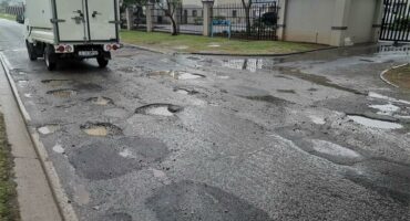 A white bakkie driving on a pothole-riddled stretch of road