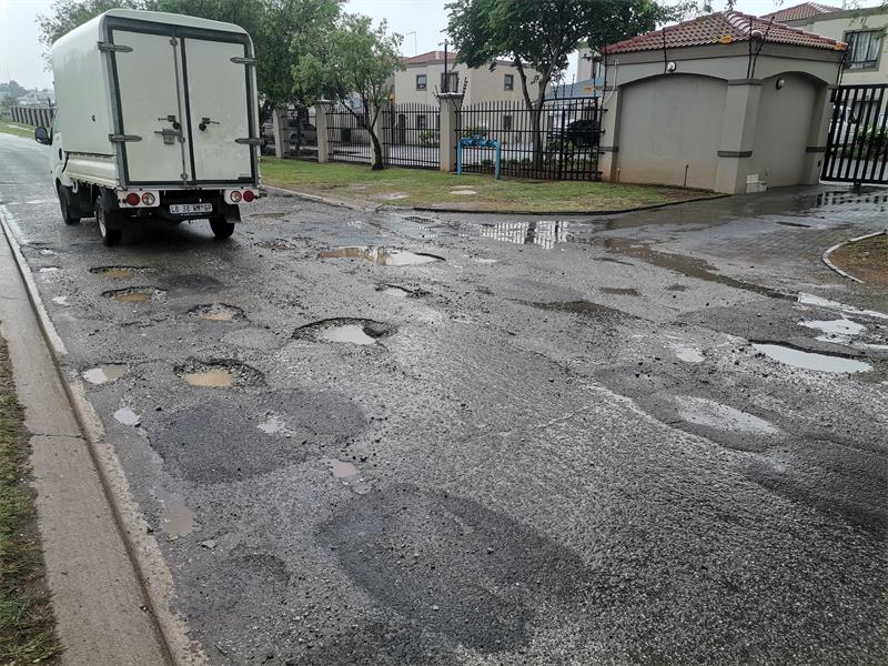 A white bakkie driving on a pothole-riddled stretch of road