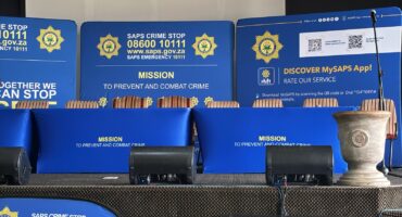 A police podium with banner and plaque featuring the official emblem, and badge of the SAPS.