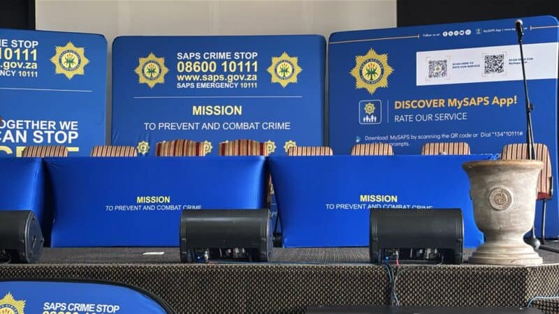 A police podium with banner and plaque featuring the official emblem, and badge of the SAPS.