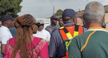 A group of people and police officers in SAPS uniform standing outside a local police station.