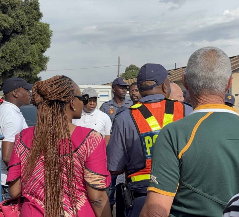 A group of people and police officers in SAPS uniform standing outside a local police station.