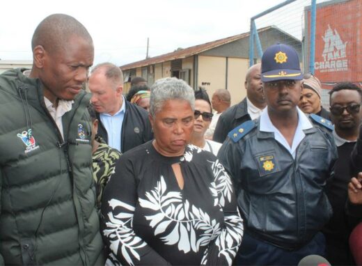 Acting Mayor Jongizizwe Dlabathi, ward councillor Edith Klassen and Reiger Park SAPS station commander Lieutenant-Colonel Lionel Chetty speaking at a press briefing, with a group of people and prefabricated offices in the background.