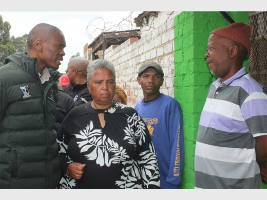 Acting Mayor Jongizizwe Dlabathi offers comfort to family of shooting victims in Reiger Park, with a green and white building 
