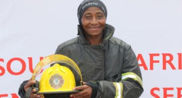 Black female firefighter in full protective gear holding her helmet.