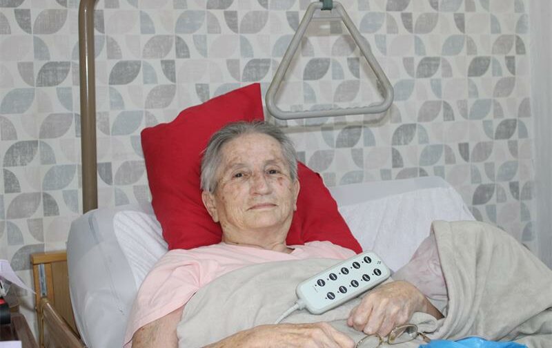 Grandmother lying in bed supported by a red pillow.