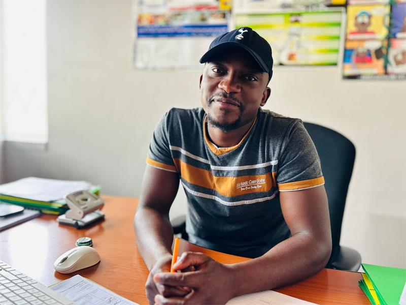 A Black man wearing a cap seated on a chair in an office
