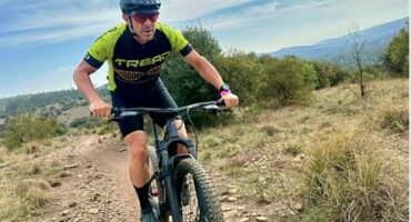White male cyclist wearing helmet and cycling outfit on a bike.