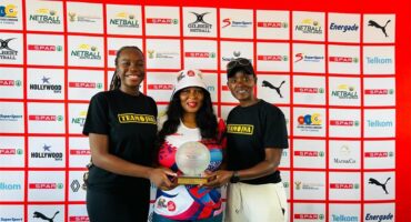 Women holding a trophy in front of a white banner,