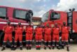 Uniformed technicians stand behind an emergency response vehicle, posing for a photo.