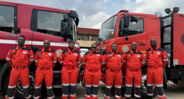 Uniformed technicians stand behind an emergency response vehicle, posing for a photo.