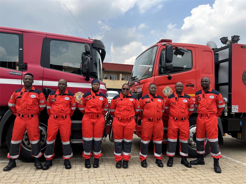 Uniformed technicians stand behind an emergency response vehicle, posing for a photo.