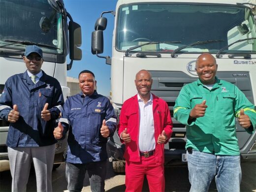 four men in work suit standing in front of waste trucks