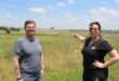 A white woman and man standing next to an open veld