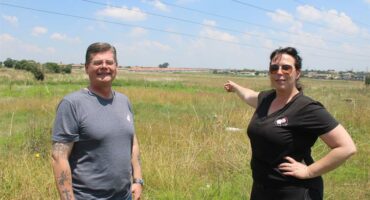 A white woman and man standing next to an open veld