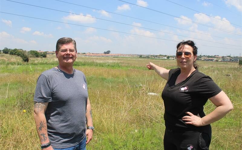 A white woman and man standing next to an open veld