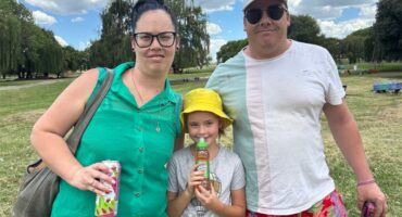 a family photo of wife, husband an a daughter standing in a park