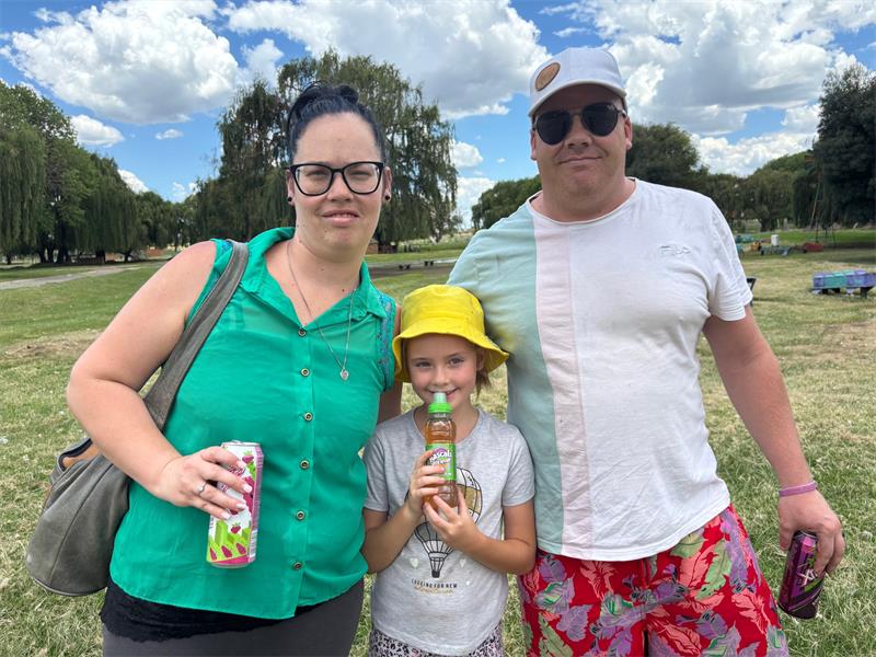 a family photo of wife, husband an a daughter standing in a park