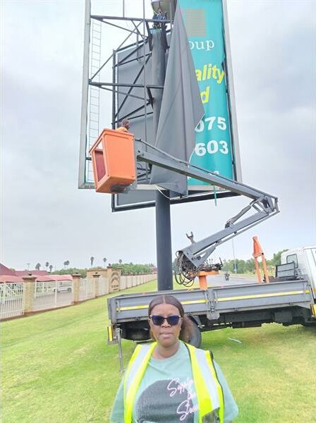 A black woman wearing reflective vest standing next to a billboard