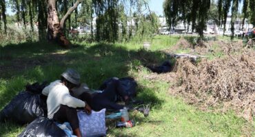 A group of men with their personal belongings sitting under a tree in a park
