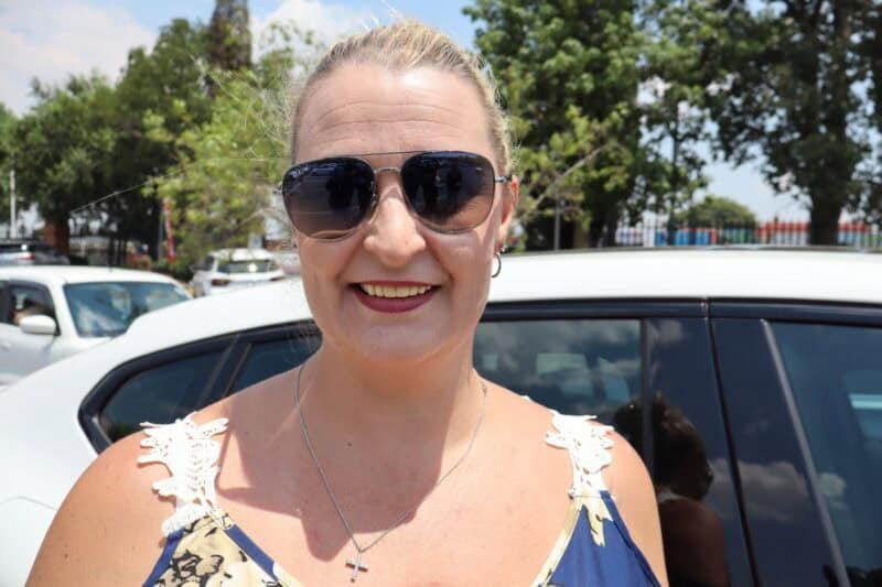 A white woman wearing glasses and standing next to a car