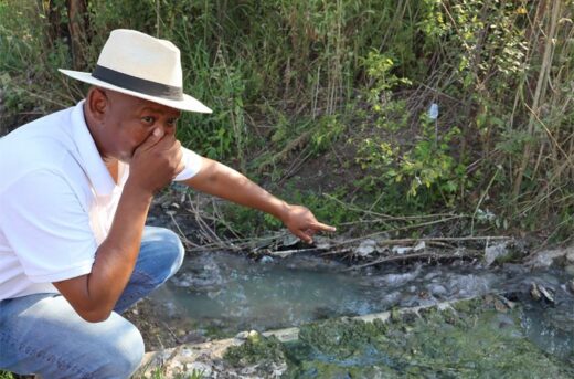 a black man standing next to a sewage spill in ekurhuleni