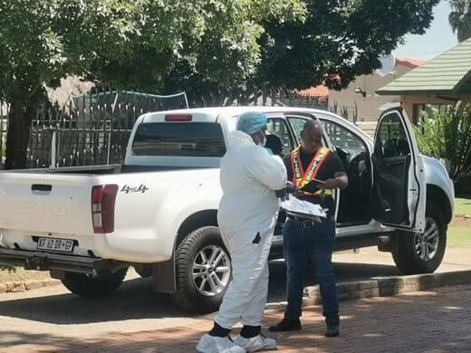 A white Isuzu bakkie riddled with bullet holes stands in a driveway of a residential area