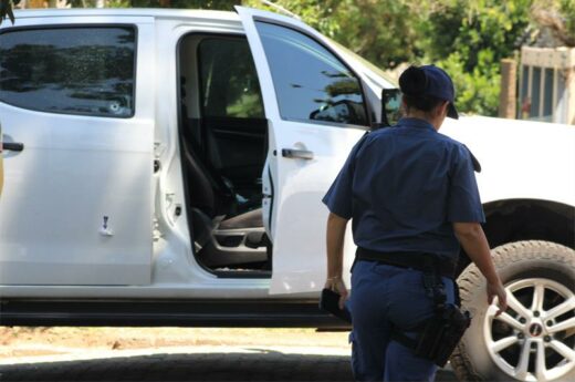 A white Isuzu bakkie riddled with bullet holes stands in a driveway of a residential area