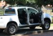 A white Isuzu bakkie riddled with bullet holes stands in a driveway of a residential area