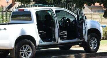 A white Isuzu bakkie riddled with bullet holes stands in a driveway of a residential area